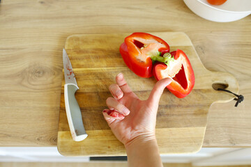 Woman cut her little finger with knife while cutting red pepper on the kitchen. Close up female...