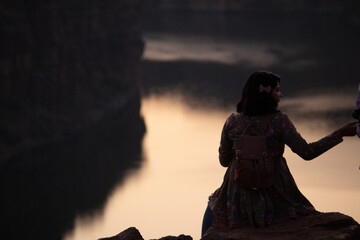 A view from the back of a tourist girl sits on a mountain and admires the beautiful view and dawn or sunset or sunrise. Woman sitting on a rock over mountains at sunrise or sunset.
