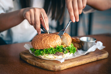 Close-up, a woman in a cafe cuts an appetizing burger.