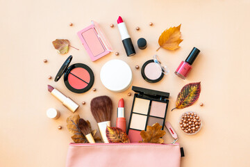 Autumn beauty background. Cosmetic bag with make-up beauty products and autumn leaves at pastel background. Flat lay with space for text.