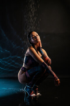 Young sexy woman poses in lingerie in BDSM style under pouring water drops.