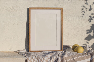 Mediterranean artistic still life. Blank vertical wooden frame picture mock up in sunlight. Cotton throw, blanket and fresh lemons fruit. White old textured wall, eucalyptus branches shadow overlay.