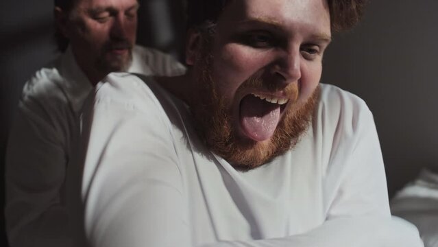Close-up shot of doctor tying up sleeves of straitjacket and pacifying patient with mental disorder