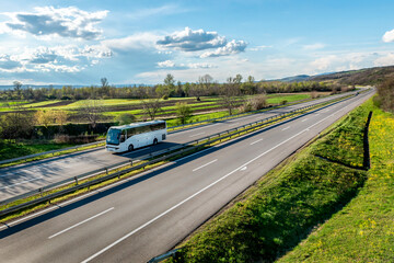 White Modern comfortable tourist bus driving through highway at bright sunny sunset. Travel and tourism concept. Trip and journey by road vehicle