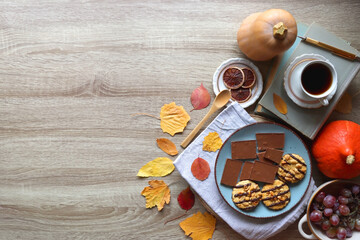 Cup of tea or coffee, plate with cookies and chocolate, dried oranges, bowl of grapes, vintage books, pumpkins and autumn leaves on the table. Autumnal hygge. Top view.
