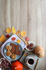 Cup of tea or coffee, plate with cookies and chocolate, dried oranges, bowl of grapes, vintage books, pumpkins and autumn leaves on the table. Autumnal hygge. Top view.