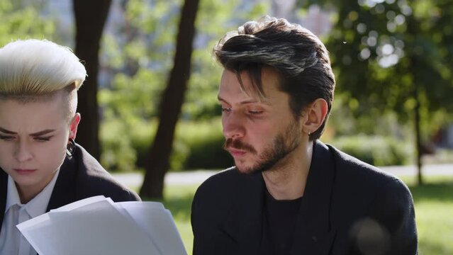 Concept Of Two Colleagues Eating Lunch Break In Park. Attorneys Speaking While Yummy Chewing Bread Check Financial Graphics Paperwork. Expertise Materials On Nature Background