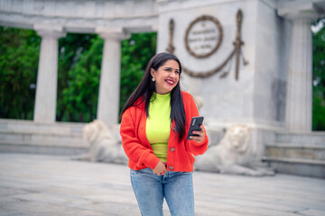 Smiling young Hispanic ethnic woman tourist smiling and looking away while standing in street with...