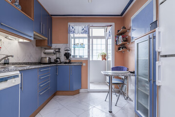 Kitchen with a wall full of plain blue cabinets with cherry wood details, gray granite countertops and stoneware floors