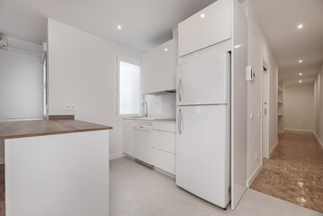 Small open kitchen with white cabinets with integrated appliances, with a peninsula with a dark wood-colored countertop and access to a long hallway