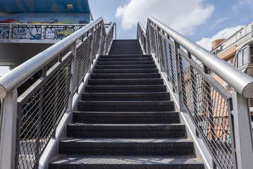 Stairs leading up to a metal walkway in an urban park next to a ring road