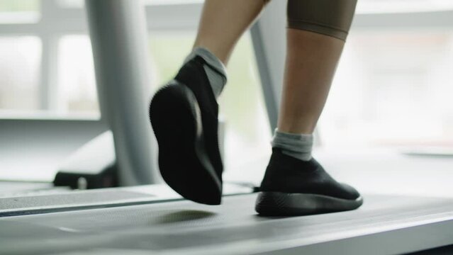 A girl athlete takes steps on a treadmill. A woman warms up her leg muscles before training. Light physical activity with using sports equipment. Close up.
