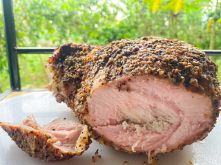 A large piece of pork smoked in a smoker against a background of nature. Smoke ring