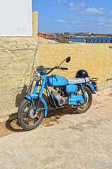 
old rusty blue motorbike leaning against the wall