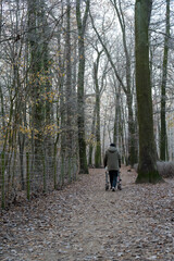 An old man walks with his walker through a frosty forest in gray morning light.