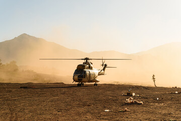 A military helicopter is seen flying and landing in desert at sunset in a cloud of dust. Air force...