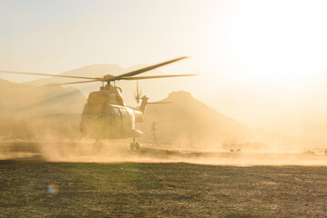 A military helicopter is seen flying and landing in desert at sunset in a cloud of dust. Air force aircraft