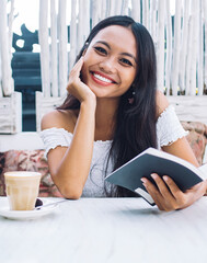 Charming ethnic female with book on cafe terrace