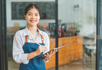 Smiling Asian coffee shop owner standing in front of cashier counter with tablet ready to take menu...