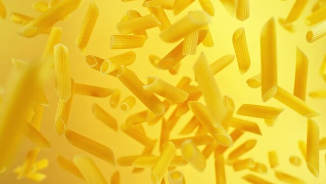Super slow motion of flying uncooked italian pasta penne on golden background. Filmed on high speed cinema camera, 1000 fps.