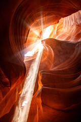 Noon in a red-orange Antelope Canyon. A thin ray of sunlight illuminates the sandy bottom of the canyon