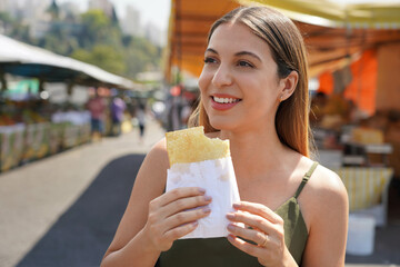 Close-up of beautiful Brazilian girl eating traditional food Pastel de Feira in Sao Paulo, Brazil