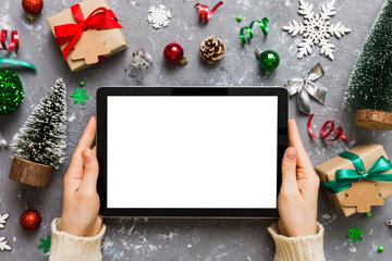 Christmas online shopping from home, female hands holding tablet pc with blank white display top view. woman hand holding tablet with blank screen, Christmas tree and gifts on background