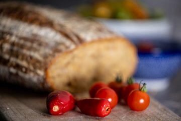 A loaf of homemade sourdough bread on a cutting board in a kitchen with homegrown chilis and homegrown tomatoes.