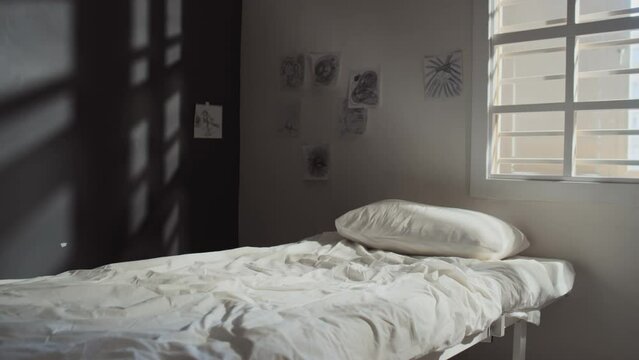 No people interior shot of ward in psychiatric hospital with bed, pencil drawings on walls and barred window