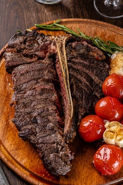 Grilled meat T-bone on the grill, cherry tomatoes lie on a wooden board. Serving food in a restaurant. background image
