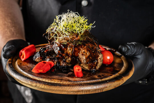 Chef holding a wooden board with a dish of fried pork meat on a dark background