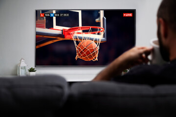 Man watching basketball match on smart TV while drinks coffee. Image of the ball entering in the hoop. Live TV transmission.