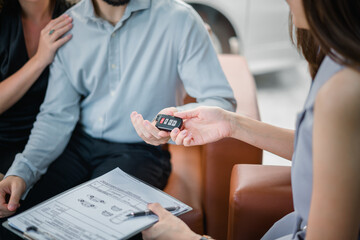 Closeup A car saleswoman gives the keys to a couple who have duly signed a purchase contract. Car rental. Car dealer. Car sales. Purchase contract and key delivery.