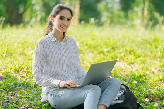 Young woman smiling and laughing with her laptop computer under a tree in the park woman studying outdoors Using a computer or video conferencing.