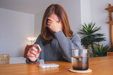 A woman holding pills while suffering from headache