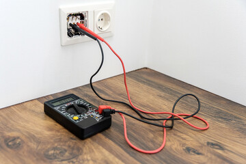a pair of wire probes are plugged into the socket. Multimeter for measuring voltage. - obrazy, fototapety, plakaty