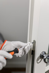 a man in white gloves holds a screwdriver and tightens the lock.