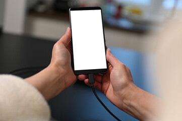 female user holding smartphone in hands, mobile phone white blank screen mockup, using mobile apps at home. - obrazy, fototapety, plakaty