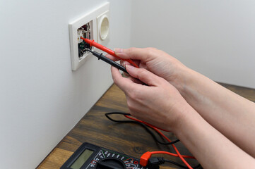 An electrical technician measures voltage using a multimeter tester. Measuring voltage in a socket.