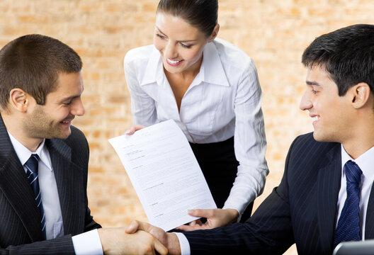 Three happy smiling successful business people handshaking with document at office.  Brown bricks wall background.