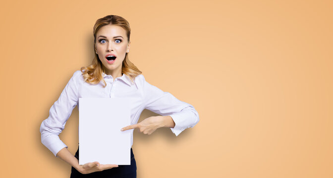 Very happy, excited surprised, astonished businesswoman with wide opened eyes, mouth, showing blank paper signboard. Success in business concept. Copy space place for text. Brown beige background.