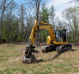 Yellow excavator at building construction site with trees in back.