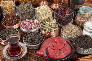 Set of different types of green, black and herbal teas next to a cast iron teapot filled with hot brewed tea on a wooden background. Delicious organic drinks. Look from above. - obrazy, fototapety, plakaty