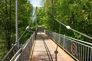 A metal pedestrian bridge over a ravine surrounded by green trees. Obninsk, Russia