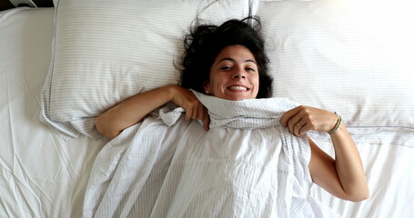Funny young woman playing hide and seek peekaboo under blanket in bed