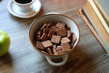 Vintage books, e-reader, pen, reading glasses, phone, cup of tea or coffee, bowl of cookies, green apple and lit candles on the table. Hygge at home, studying atmosphere. Selective focus.