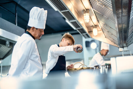 Senior male chef teaches young teenage boys cooking in school kitchen. Education Concept