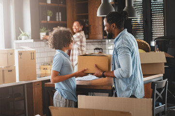 Happy young African-American family husband, wife, and teen son just moved into a new home...