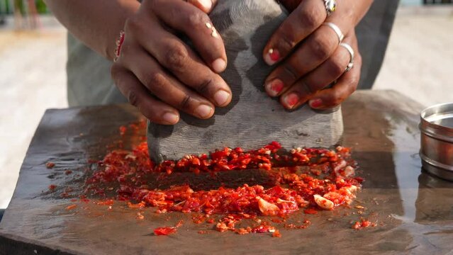 Woman's hand Grinding chili with stone or manual process of making chili sauce. Indian spices for hot and spicy curry, cuisine and dish.
