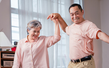 Fototapeta premium Asian sweet senior elderly couple wearing casual clothes, staying in indoor cozy home at living room, dancing together with happiness and passion, smiling. Retirement, Lifestyle, Healthcare Concept.